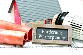 Holzschild mit der Aufschrift Förderung Wärmepumpe vor einem Hausmodell